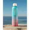 Sunscreen spray bottle on sand with ocean background