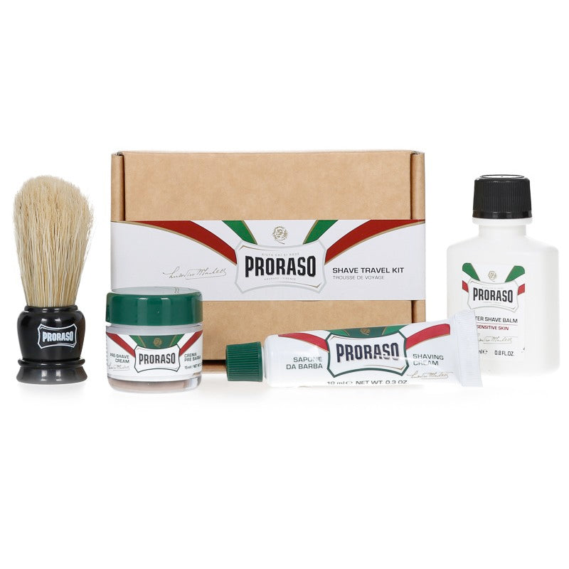 Proraso travel shaving kit set, including a shaving brush, pre-shave cream, shaving cream in a tube, after shave balm, and a bottle of water, all displayed in front of a cardboard box with the Proraso brand and 'Travel Shaving Kit' text.