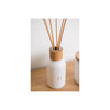 White diffuser bottle with wooden top and reeds on a light surface