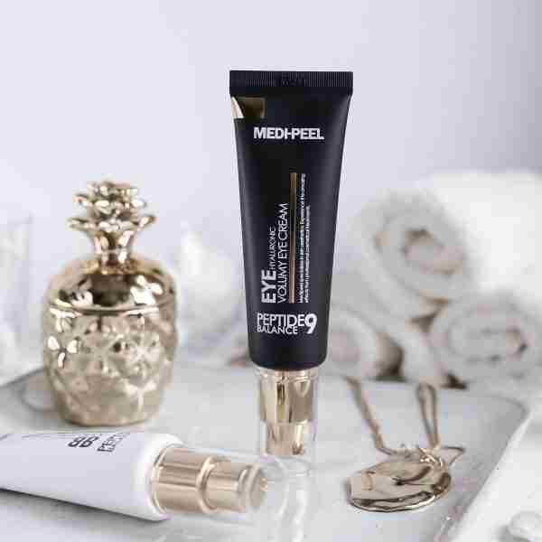 Medi-Peel eye cream tube on a white surface with decorative items.