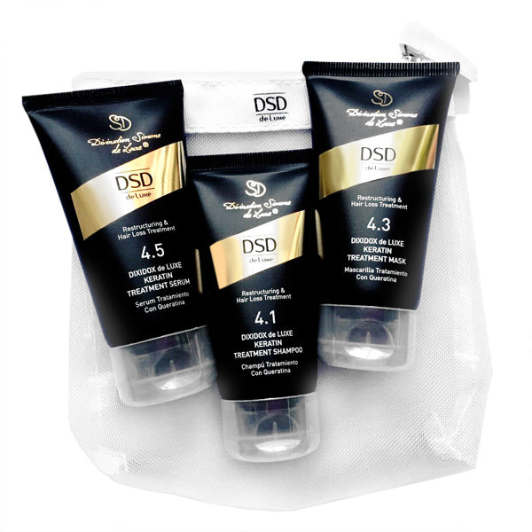 A travel set of DSD de Luxe hair care products including shampoo, hair mask, and hair serum, packaged in black tubes with gold and white accents, displayed in front of a gray background.