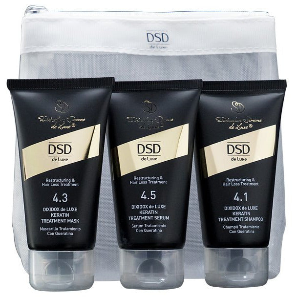 A travel set of DSD de Luxe hair care products including shampoo, hair mask, and hair serum, packaged in black tubes with gold and white accents, displayed in front of a gray background.