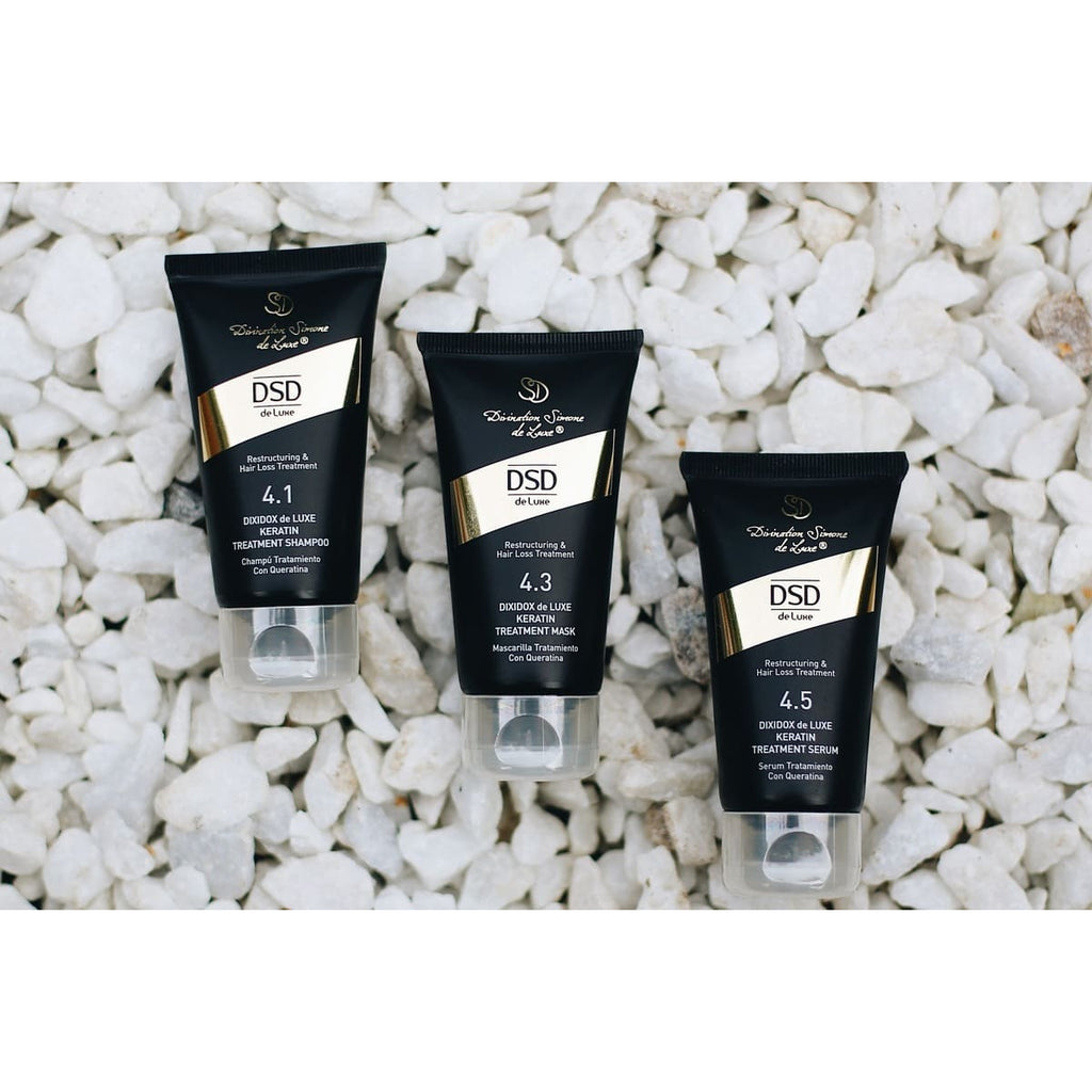 A travel set of DSD de Luxe hair care products including shampoo, hair mask, and hair serum, packaged in black tubes with gold and white accents