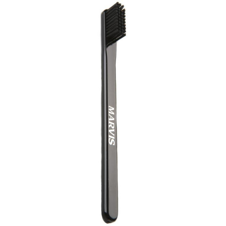 A black manual toothbrush with bristles, featuring a cap and the MARVIS brand name on the handle.